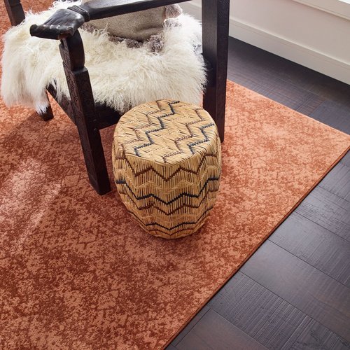 Wooden armchair in a room with dark hardwood flooring and a large orang patterned are rug - Carpet binding services from Carpet Innovations in Denver, CO